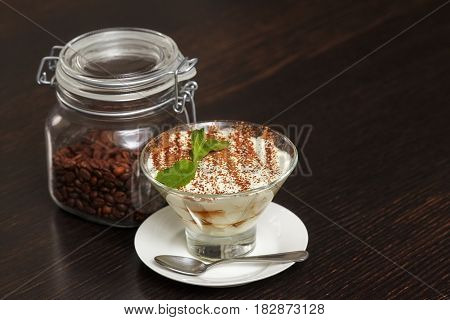 Tiramisu creme cake dessert in glass with mint leaves and coffee beans on black wooden background