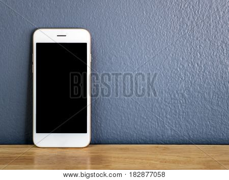 Front view image of white smartphone leaning against the gray wall on wooden table with copy space