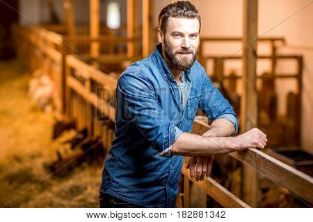Portrait of a handsome businessman farmer standing in the barn with goats. Natural milk production and farming