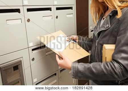 Close-up picture of woman's hands holding envelopes and package next to the mailboxes