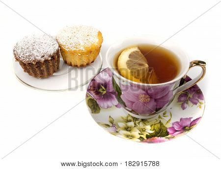 Mug of tea with lemon and and two cupcakes on isolated white background