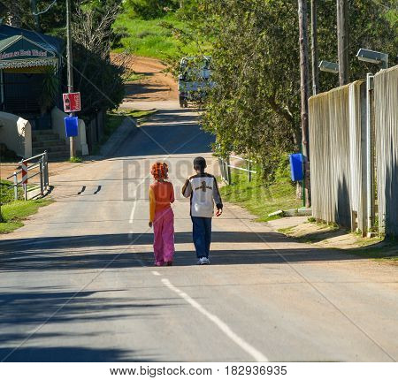 Maun, Botswana - August 28, 2007; Two black children in colorful clothes walking together away on country road in South Africa.