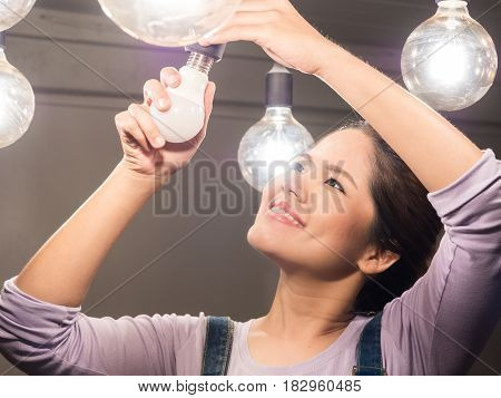 asian woman wearing jumpsuit changing light bulb