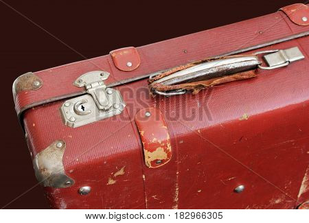 Closeup of battered old red suitcase against dark background