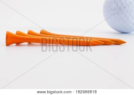 Orange wooden golf tees and golf ball on the white table