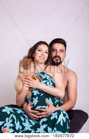 Happu pregnant woman with her husband and dog in studio photo. Wife and husband. Parenthood and expecting baby