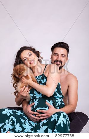 Happu pregnant woman with her husband and dog in studio photo. Wife and husband. Parenthood and expecting baby