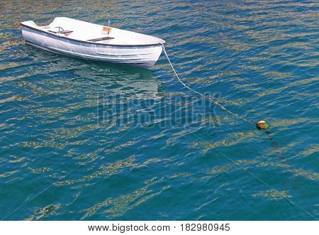 little white rowing boat anchored in blue and green water sunlight reflections