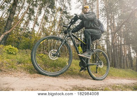 Young attractive man wears dark suit ride the bike on the forest road