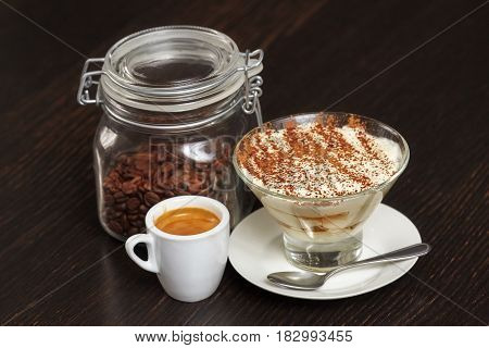 Tiramisu creme cake dessert in glass with mint leaves and coffee cup on black wooden background