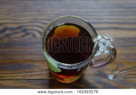 Black hot tea in a big cup and cherry flowers on right side of tea cup. Selective focus