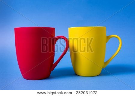 Big Yellow And Red Mugs Isolated On Blue Background, Horizontal Orientation.