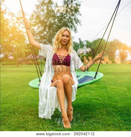 Youmg Beautiful Woman In Beautiful Summer Garden Is Round Swing