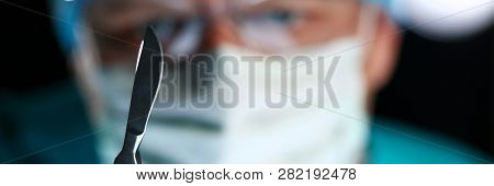 Surgeon Arms In Sterile Uniform Holding Sharp Knife While Operating Patient In Surgical Theatre Clos
