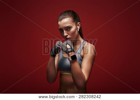 Modern Athlete. Sportswoman Standing Concentrated In Gym Gloves Over Red Background.