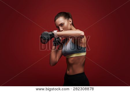 Train Insane Or Remain The Same. Sportswoman Is Training With Dumbbells Standing Over Red Background