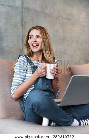 Adult Happy Woman Sitting With Cup And Laptop On Pink Sofa