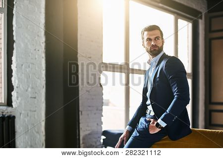 Fashion Portrait. Young Bearded Successful Businessman In Stylish Suit Is Standing At Office And Thi