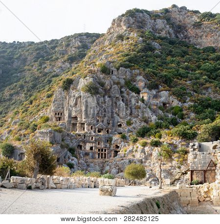 Ancient Lycian Necropolis With Tombs Carved In Rocks. Tourists Walking Near Lycian Tombs In Mira.