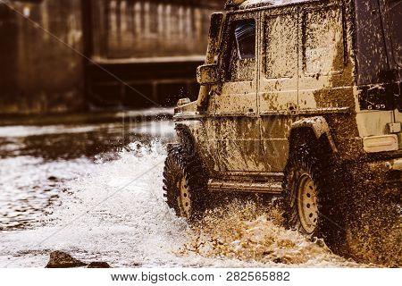 Mud And Water Splash In Off The Road Racing. Bottom View To Big Offroad Car Wheel On Country Road An