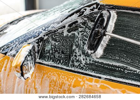 Yellow Car Side Window Washed In Self Service Carwash. Rush Leaves Strokes In Shampoo And Foam On Gl