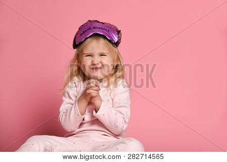 Studio Shot Of Pleased Beautiful Young Woman Posing In Eyemask. Cheerful Little Cute Girl In Pajamas