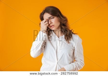 Upset young woman casualy dressed standing isolated over yellow background, suffering from a headache