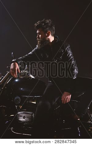 Man With Beard, Biker In Leather Jacket Lean On Motor Bike In Darkness, Black Background. Brutality 