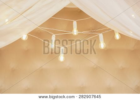 Garland Of Light Bulbs Hanging Against A Beige Wall With Curtains