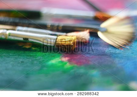 The Fluffy Brush Lies On The Palette Painted With Multi-colored Oil Along With Other Brushes