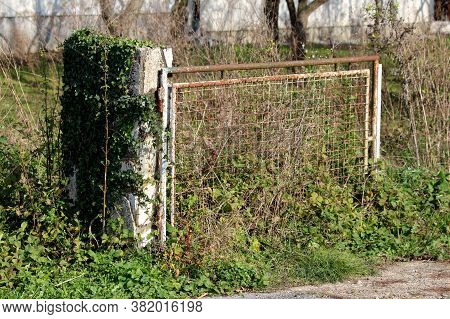 Rusted White Metal Front Yard Entrance Doors Mounted On Dilapidated Cracked Concrete Wall Surrounded