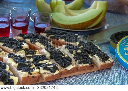 Black Caviar On A Piece Of Bread With Slices Of Butter On A Melon Background