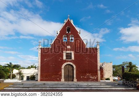 Entrance Of The Red Colonial Church Itzimna In A Sunny Park With Trees, Merida, Yucatan, Mexico