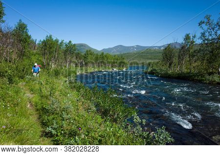 Hiking in Sweden in summer. Man traveler trekking alone along river in Abisko National Park in northern Sweden. Arctic nature of Scandinavia in warm sunny day with blue sky
