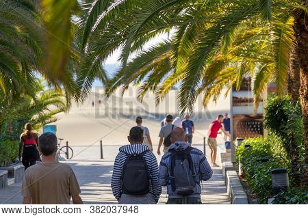 Playa Del Ingles, Spain - 5 Jan, 2020: Tourists Are Walking Toward Famous Maspalomas Dunes Beneath T