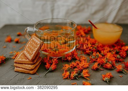 Tea With Calendula Flowers And Biscuits. Transparent Glass Cup And Saucer