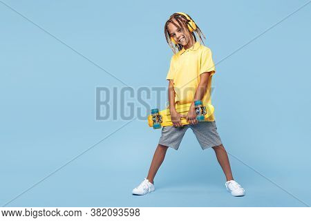 Stylish Confident Little Boy With African Dreads With Headphone And Skateboard Posing Over Blue Back
