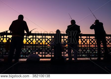 Unidentified turkish fishermen silhouette on Galata bridge with Galata tower at background at twilight in Istanbul