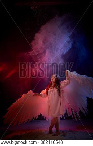 Small Young Model Girl With White Wings Posing And Dancing In Dark Black Studo During Photoshoot Wit