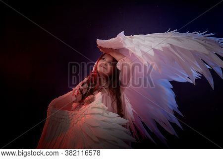 Small Young Model Girl With White Wings Posing And Dancing In Dark Black Studo During Photoshoot Wit