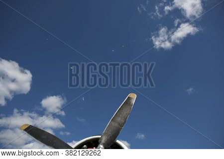 The Proppelers Of A Vintage Aircraft And A Group Of Paratroopesr In The Blue Sky