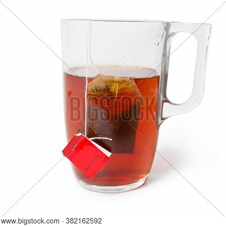 Bag Of Black Tea With Red Label In The Glass Cup With Freshly Brewed Tea On A White Background Close