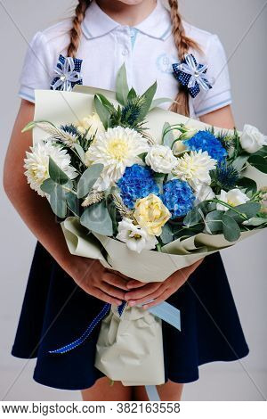 A Bouquet Of Flowers, Packed In Beige Paper In The Hands Of A Girl With Pigtails On A Light Backgrou