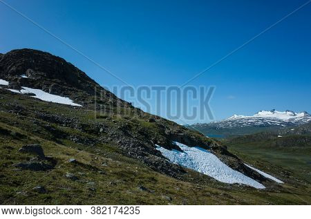 Snow on slope of Stuor Allagas hill in Swedish Lapland, Arctic nature of Scandinavia in warm summer sunny day with blue sky