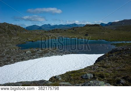 Snow and water on Stuor Allagas hill in Swedish Lapland, Arctic nature of Scandinavia in warm summer sunny day with blue sky