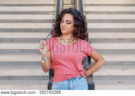 Young Women Wearing T-shirt And Jeans Stays Near The Stairs And Touch Hairs