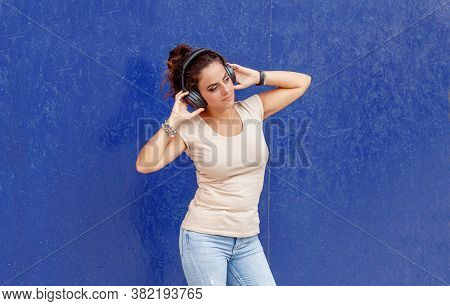 Young Women Listening Music With Headphones Near A Blue  Wall