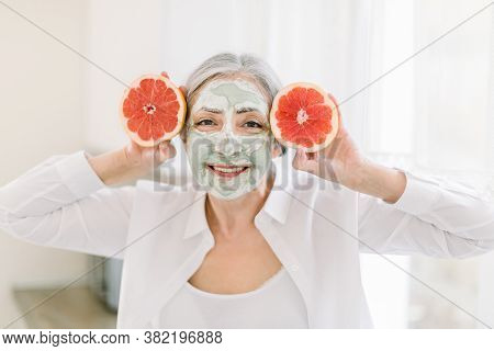 Close Up Beauty Portrait Of Pretty Elderly Grai Haired Woman With Mud Clay Facial Mask, Holding Near