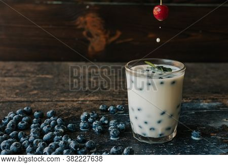 A Womans Hand Holds A Cherry And Soaks It In Milk. Blueberries Are Scattered