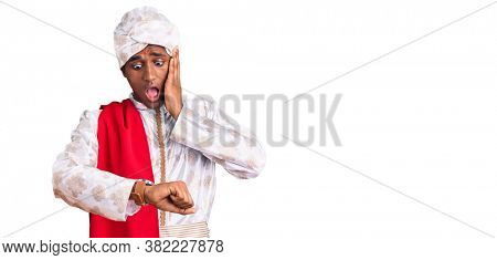 African handsome man wearing tradition sherwani saree clothes looking at the watch time worried, afraid of getting late 